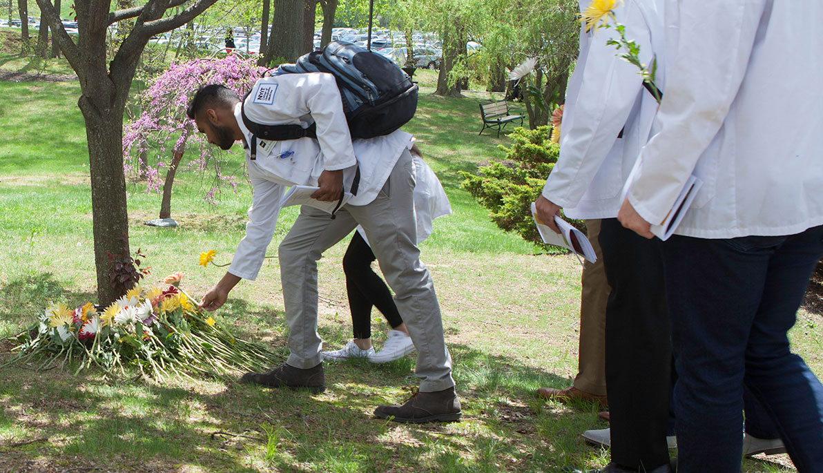 NYIT student placing flower by tree