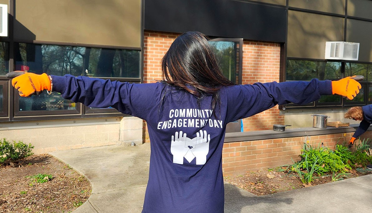Person with arms stretched out wearing t-shirt that reads Community Engagement Day