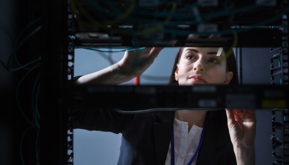 View of young woman through electronic equipment as she checks network wires