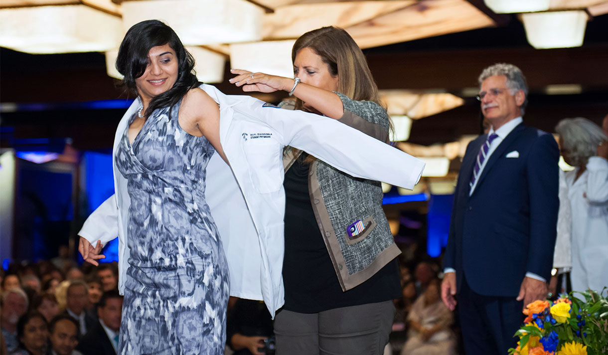 Female student receiving white coat from faculty member 