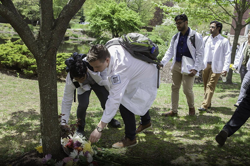 Students place flowers near the base of a newly planted tree dedicated in memory of those who donated their bodies to science.