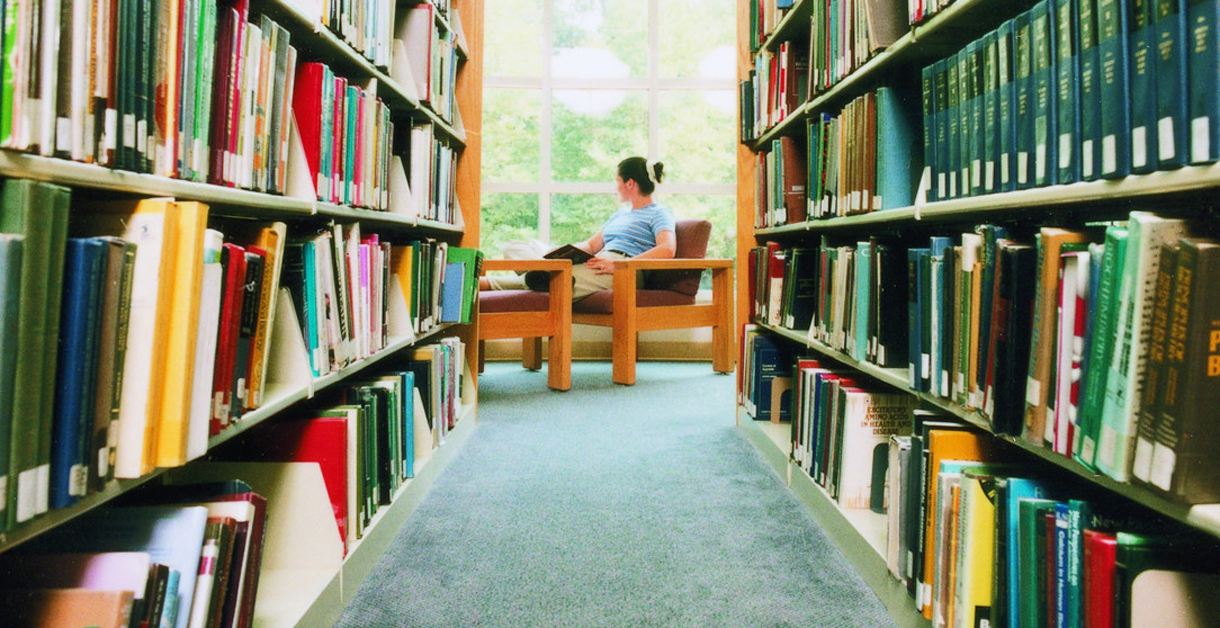Student sitting in bookstacks of library