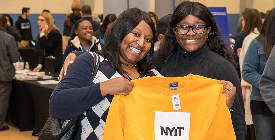 Two women holding up a yellow NYIT t-shirt