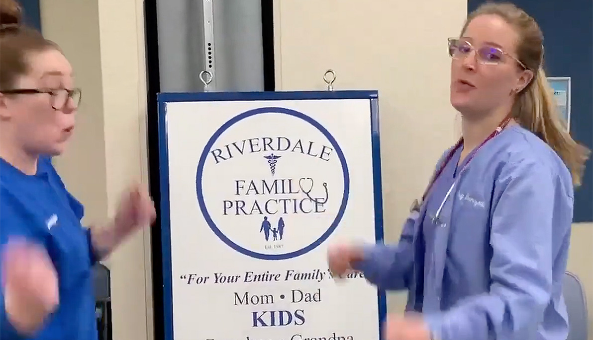 NYITCOM student Megan Franzetti dancing in her scrubs with a colleague in front of Riverdale Family Practice sign