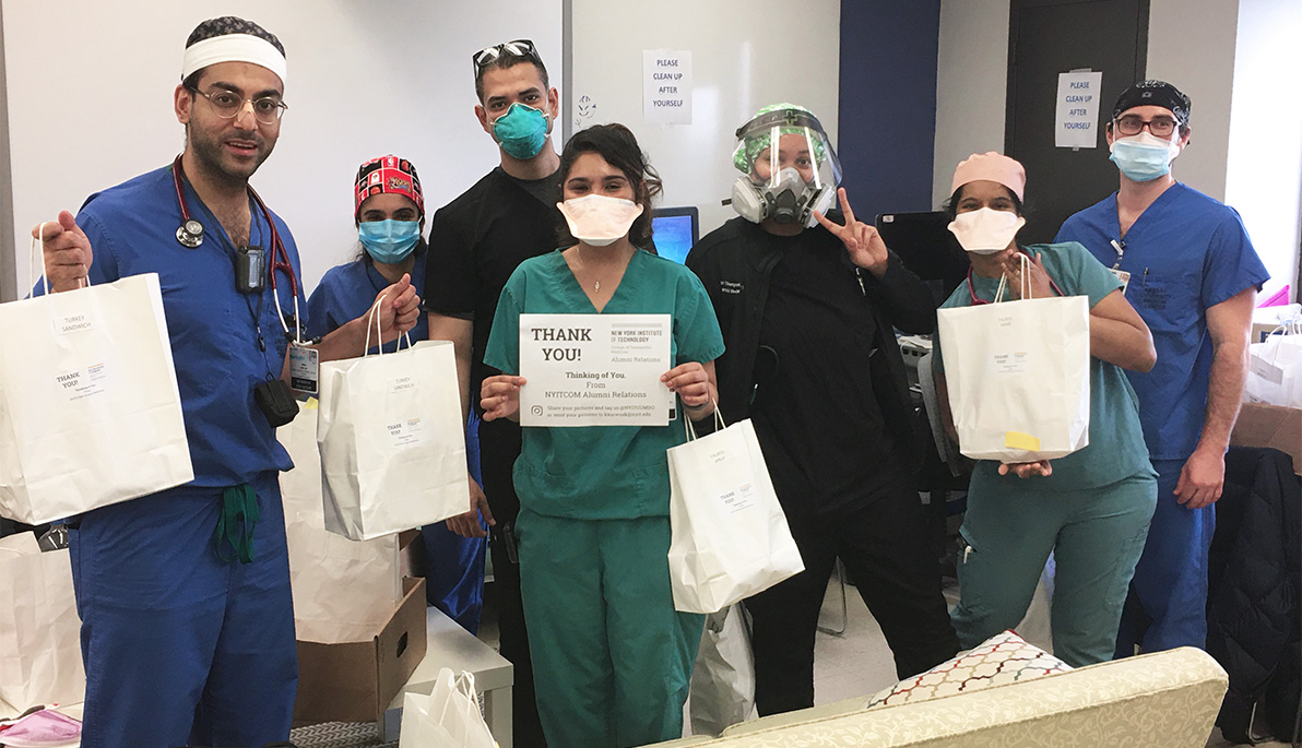 Medical workers in scrubs and face masks hold bags of food delivered by NYITCOM alumni.