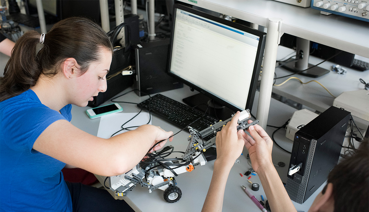 A young high school student works on a robotic arm.