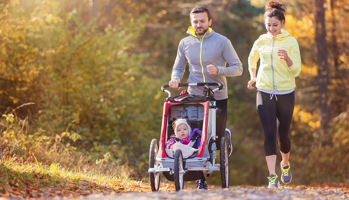 Two parents jogging with their baby in a stroller.