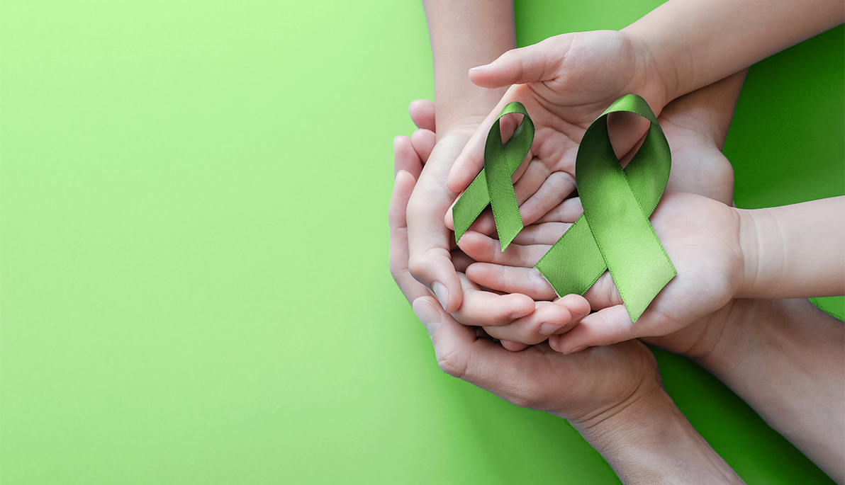 Close-up of hands holding lime mental health awareness green ribbons.