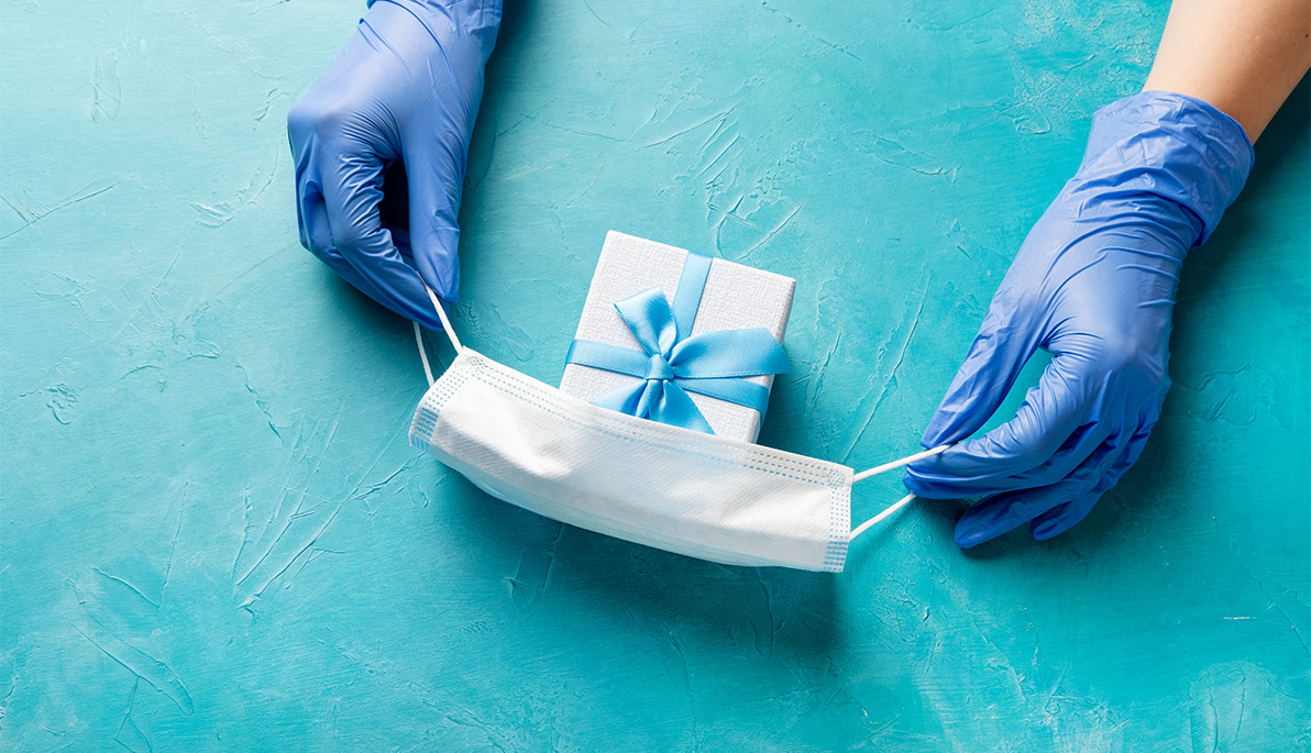 Gloved hands placing a surgical mask over a wrapped gift.