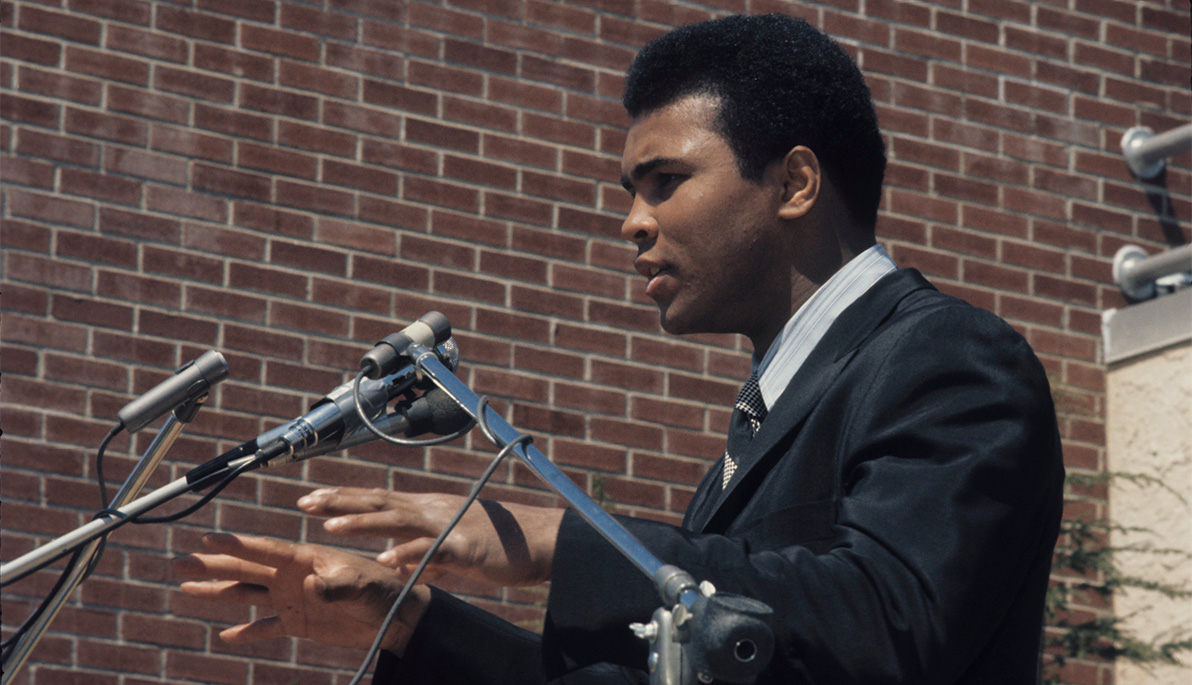 Muhammad Ali speaking at a podium on the New York Tech Long Island campus.