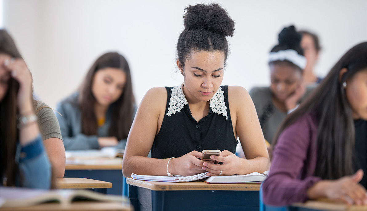 Student sitting at her desk in the classroom looking at a smart phone