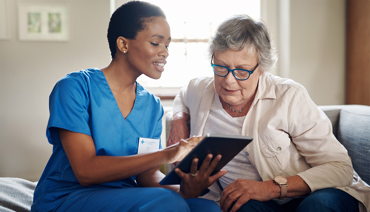 Healthcare aid looking at a tablet with an elderly woman.