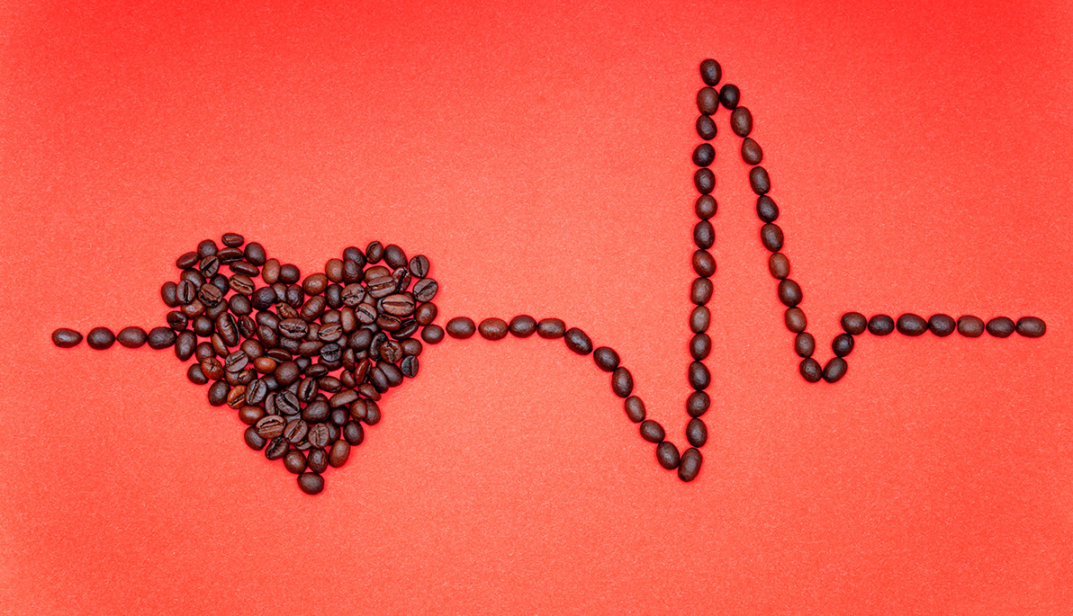 Heart symbol and a heart rate line made of roasted coffee beans arranged on a red background.