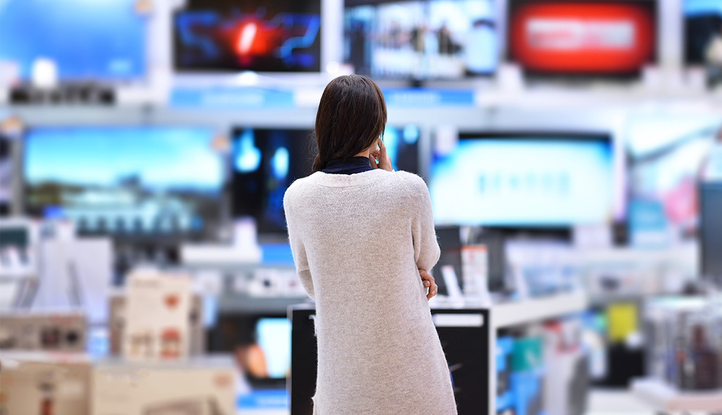 a woman in a store looks at various televisions