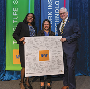 Melanie Austin (B.S. ’00) (left), Lexi Ruiz, and President Foley hold up a poster signed by well-wishers at the kickoff event.