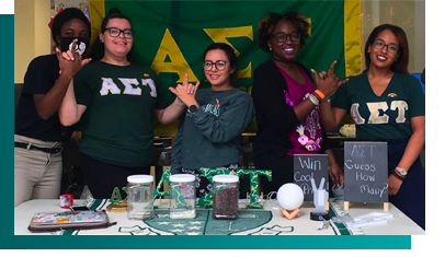 students from Alpha Sigma Tau sorority standing behind contest table
