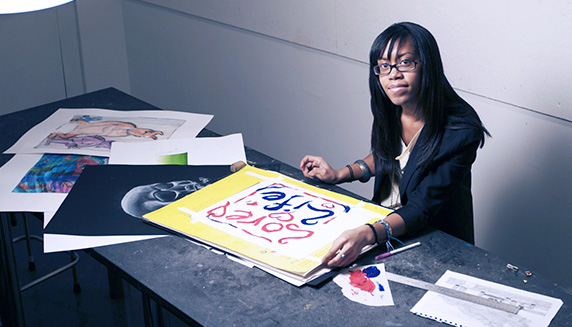 Graphic Design student using paint sample cards to decide the best color for a poster on the computer