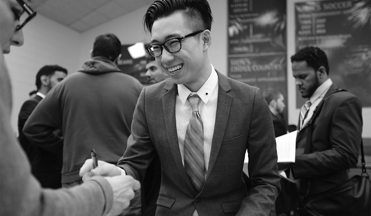Student in a tie and jacket talking to a recruiter at a job fair