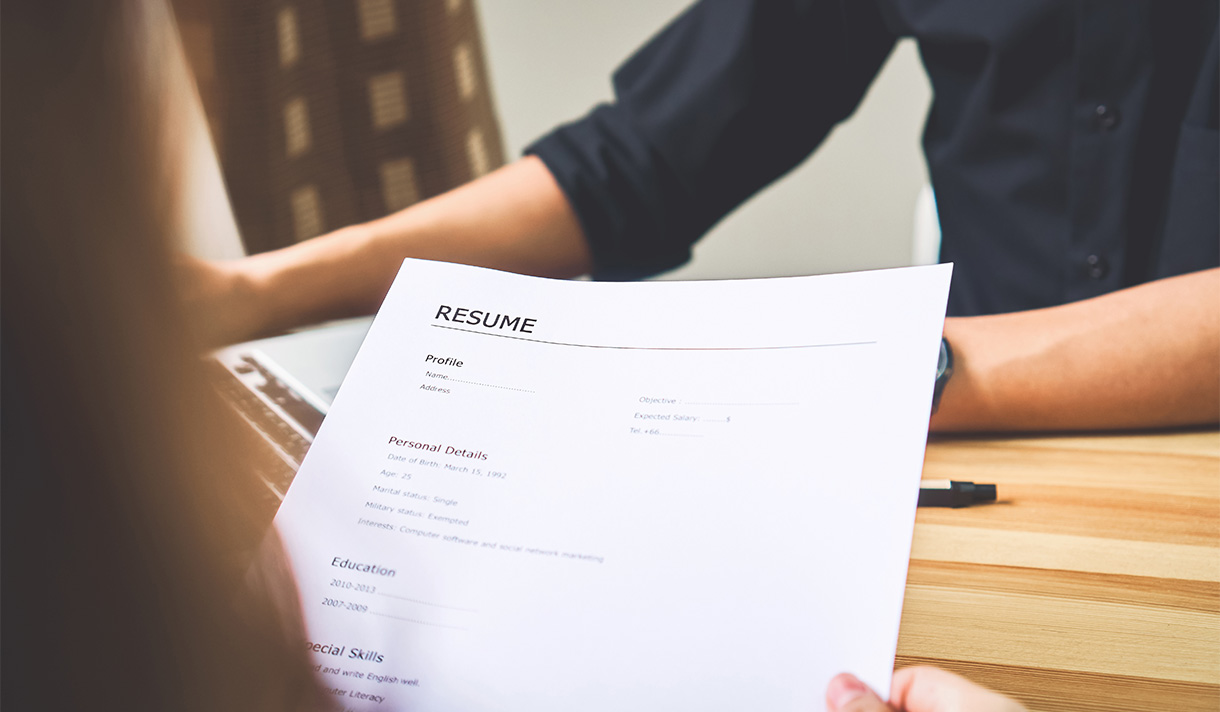 Close up of employer holding a resume across the desk from a potential employee