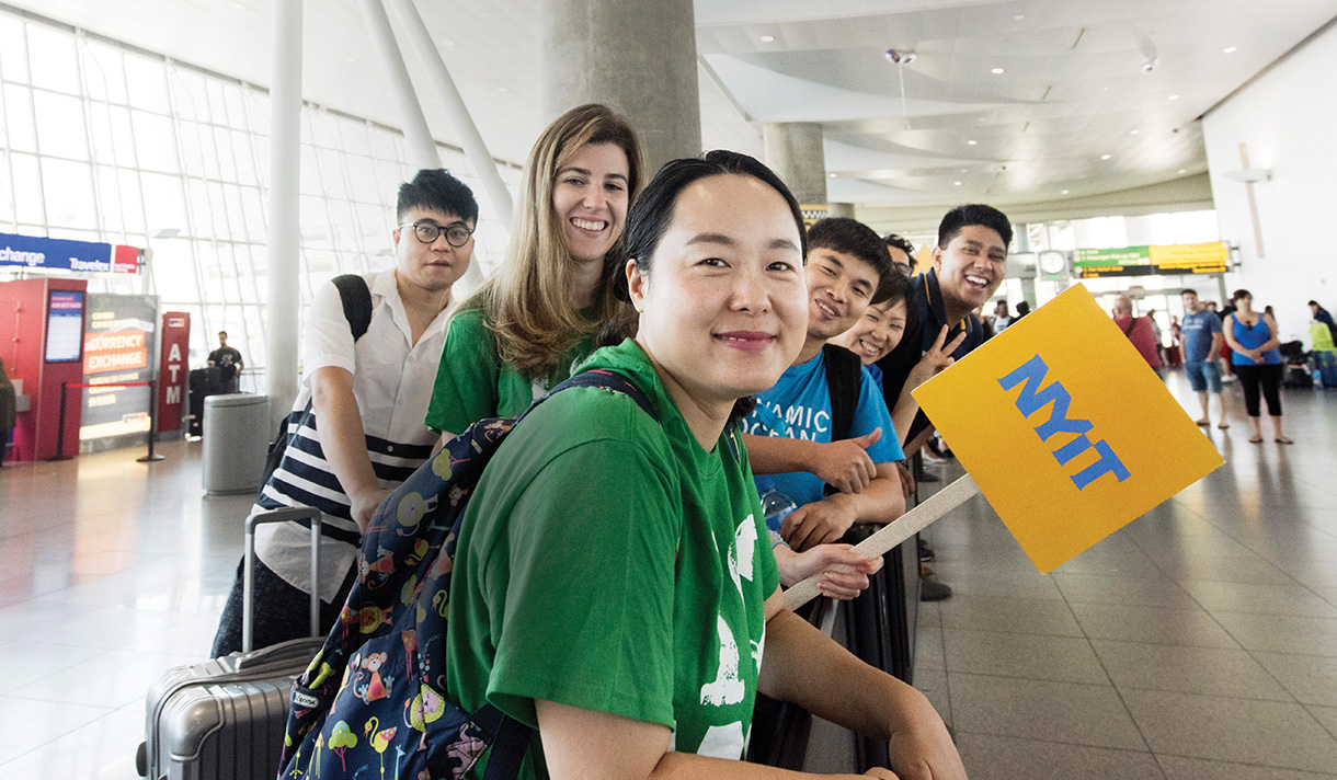 Group of NYIT International Students waiting at the airport holding an NYIT sign.