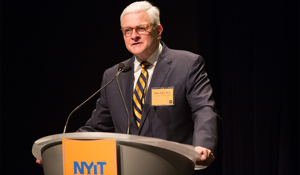 President Foley addresses a crowd from behind an NYIT podium.