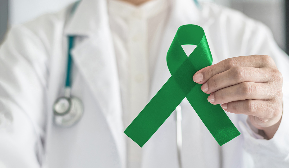 Doctor in white coat holding green bone marrow donation awareness ribbon