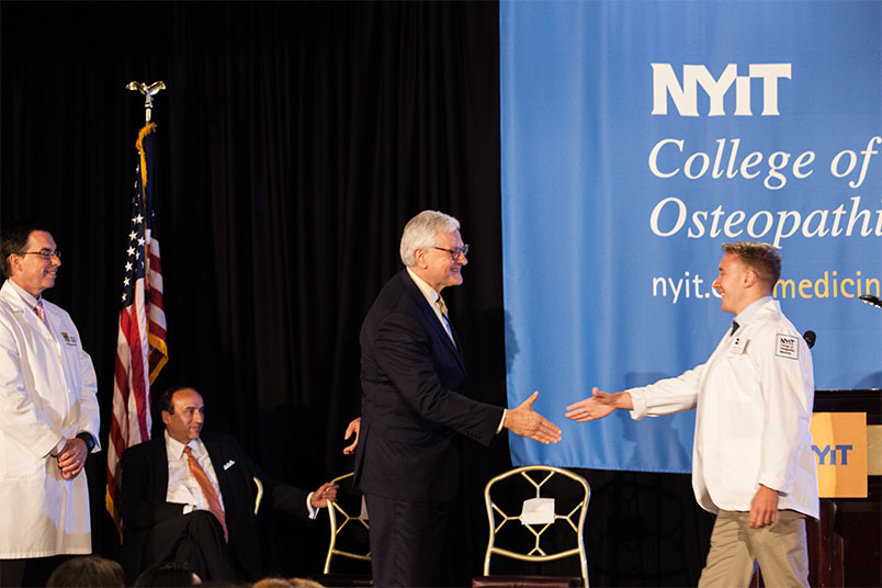 NYIT President Hank Foley shakes hands with a newly coated medical student.