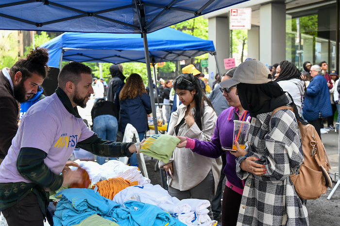 Dean of Students Felipe Henao hands out free t-shirts, bucket hats, and cup holders to all those who checked in at the New York City Street Fair.