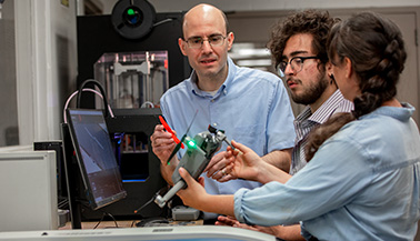 Two New York Institute of Technology students and faculty member looking at device