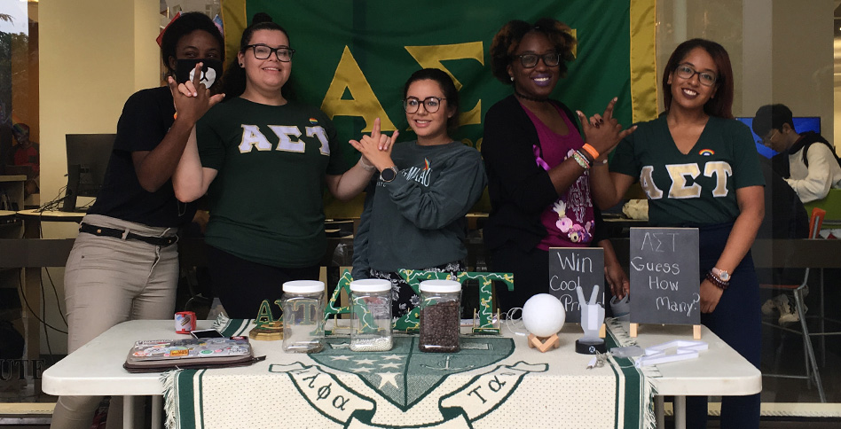female students from Epsilon Iota chapter of Alpha Sigma Tao run contest at table on campus