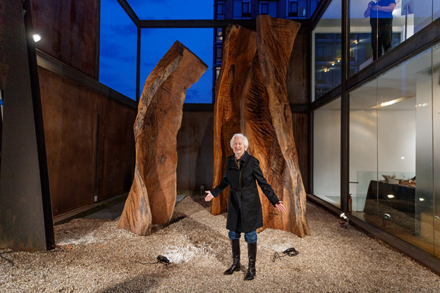 Artist Emilie Brzezinski standing in front of finished sculpture of three wooden beams