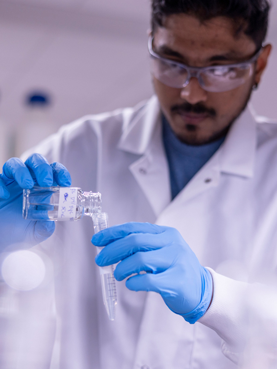 A researcher wears blue gloves and pours liquid into lap equipment.