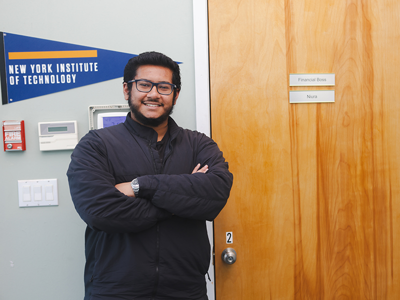 New York Tech student Ryan Ahmed poses in front of an office door for his startup company.