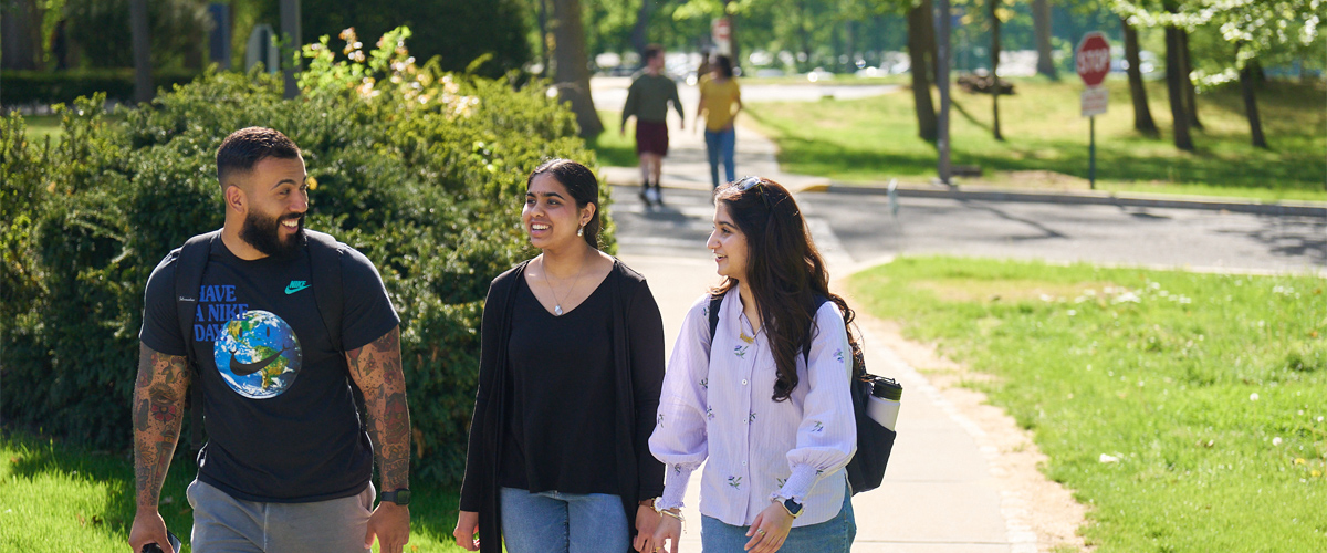 Three students walking at the Long Island campus on a grassy pathway.