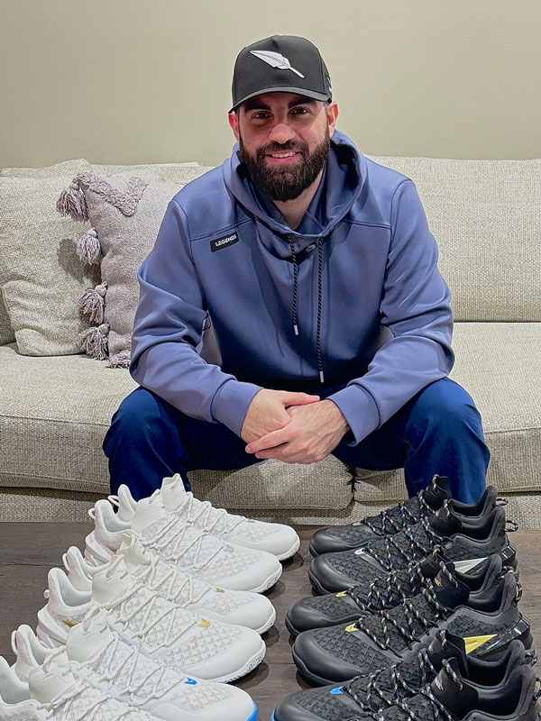 A student poses with a row of white sneakers and a row of black sneakers to showcase his business.