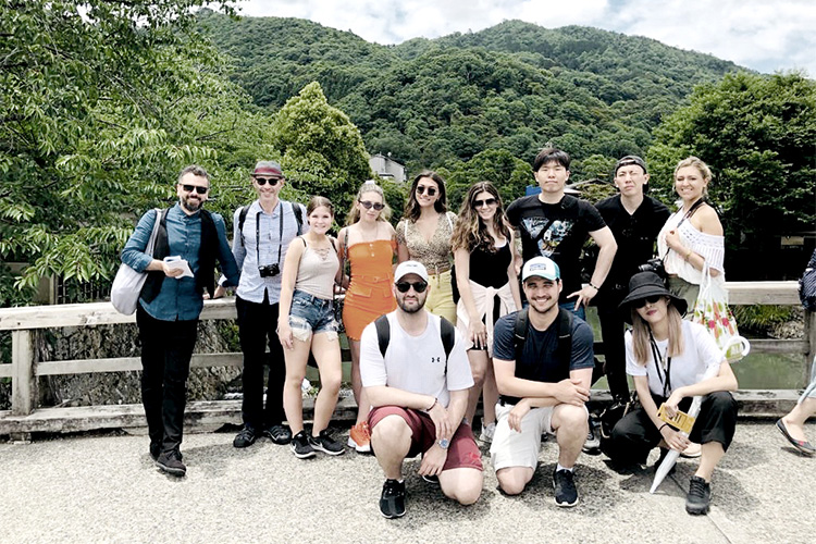 A photo of a group of study-abroad students posing for a photo on a bridge with a lush green mountain in the background.