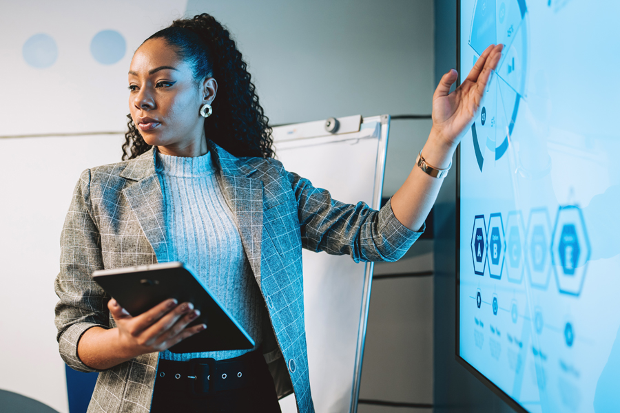A woman holding a tablet while showing graphs on a tv display in a classroom