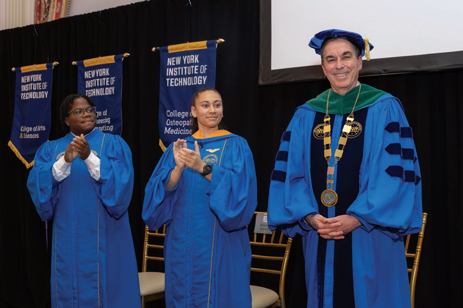 President Balentine smiles on stage during his inauguration ceremony with two students.