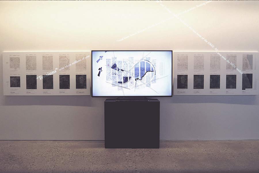 A gallery with art arranged in a grid with a tv screen in the middle presenting