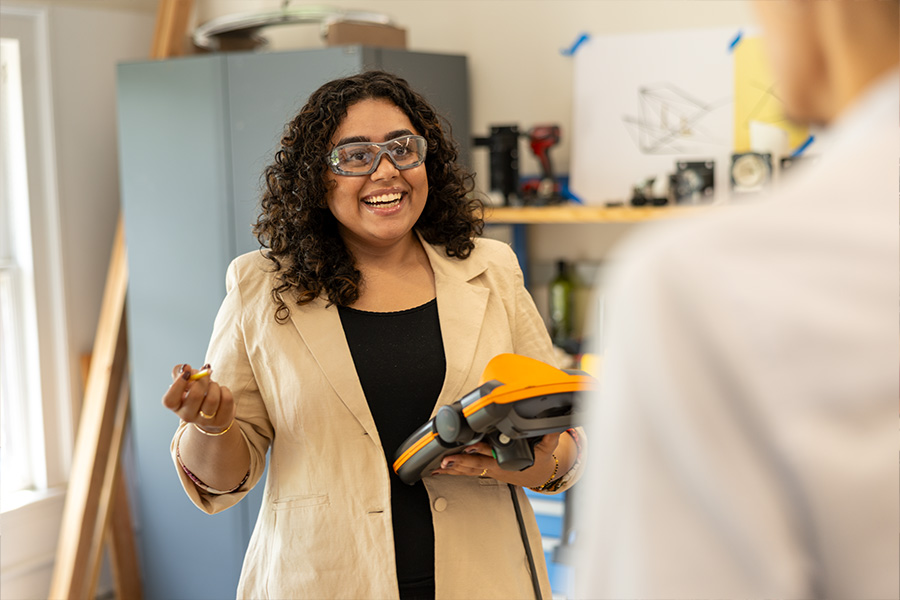 Smiling woman in yellow coat holding a tablet talks to a man with his back to the camera.