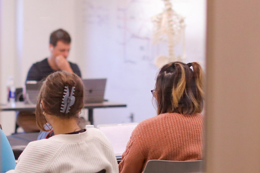 Back of students heads in a classroom looking at the front of the class where a skeleton diorama is.