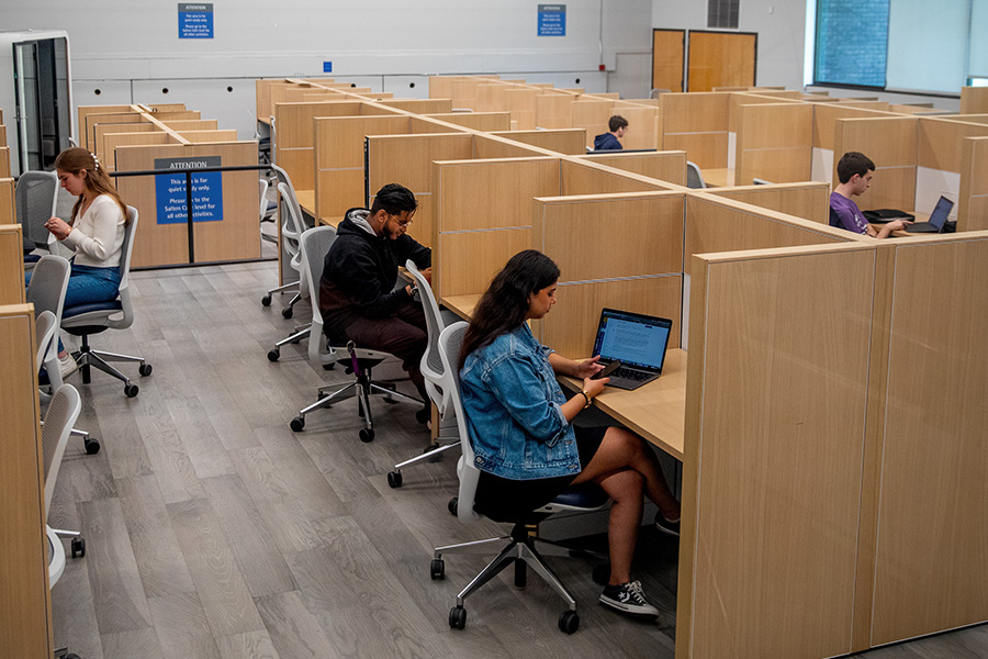 Students studying on laptops in cubicles.