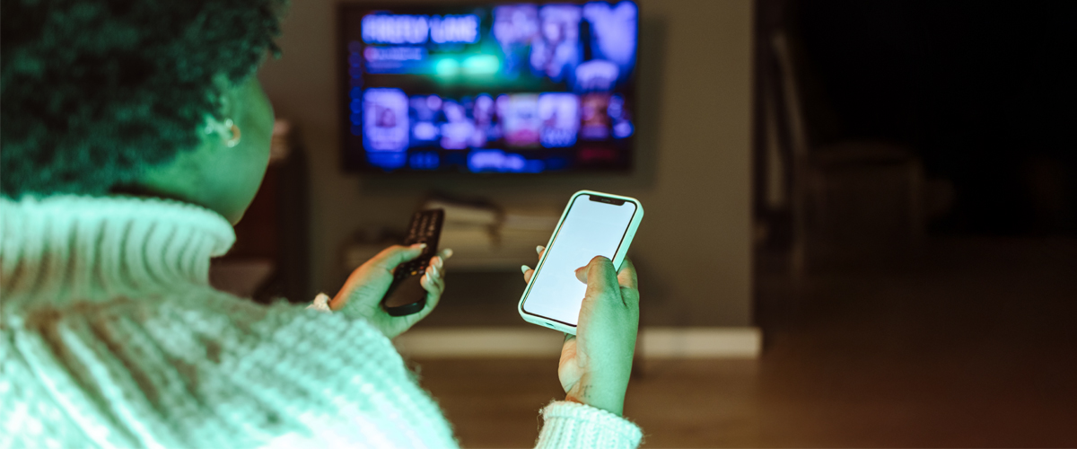 Woman watching tv and holding a phone and remote control
