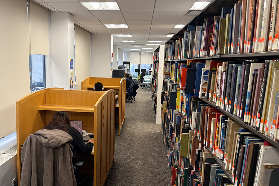 Students studying in cubicles along a bookshelf.