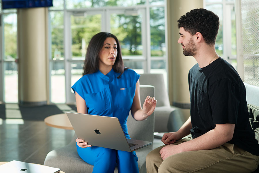Two people talk about content shown on a laptop.