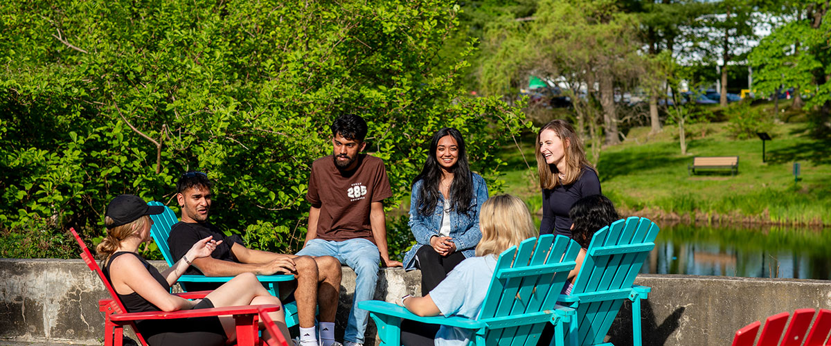A group of students are sitting and chatting in coloring Adironack chairs.