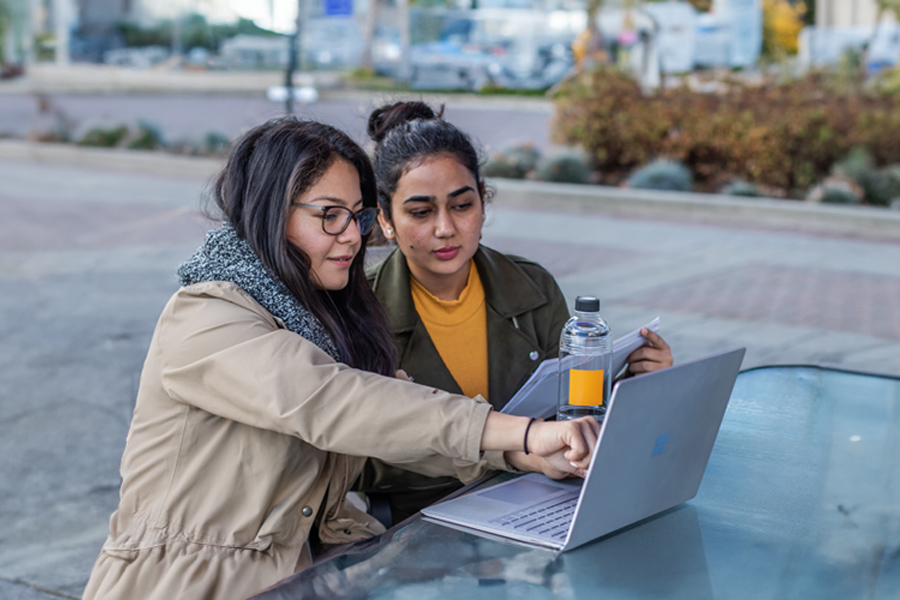 Two female students outside. One pointing at a computer screen.