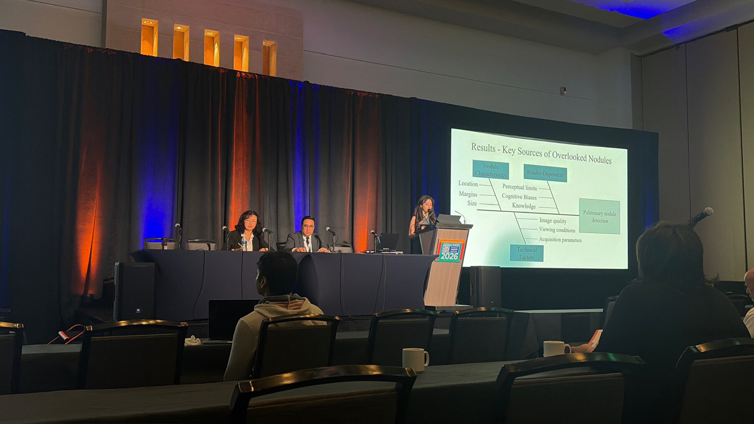 Talia Lilikakis speaking at a podium next to a screen