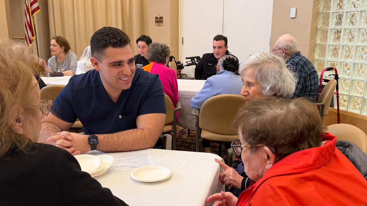 NYITCOM student sitting at a table with assisted living residents