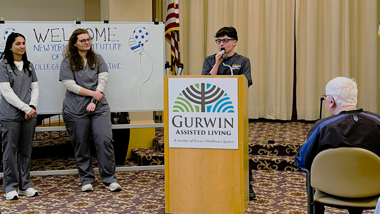 NYITCOM student speaking at podium while two classmates look on